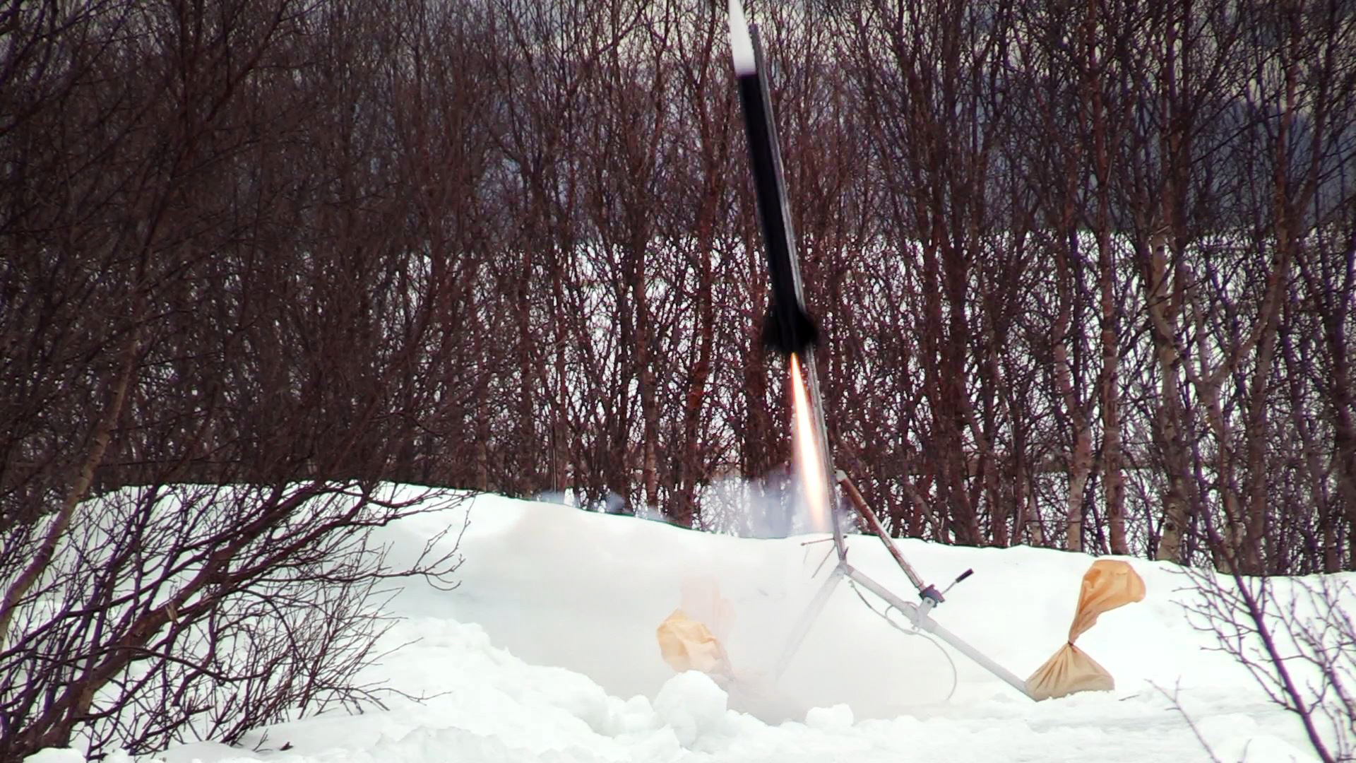 En rakett blir skutt opp fra en rampe utendørs med trær og snø i for- og bakgrunn.