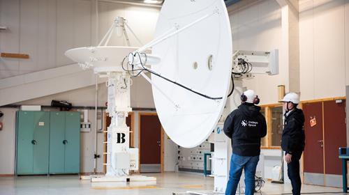 To mennesker som står ved siden av en stor parabolantenne inne på et lager.