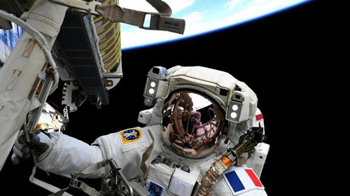 En astronaut ute på romvandringen. Jorden sees i bakgrunnen og astronauten holder seg fast.